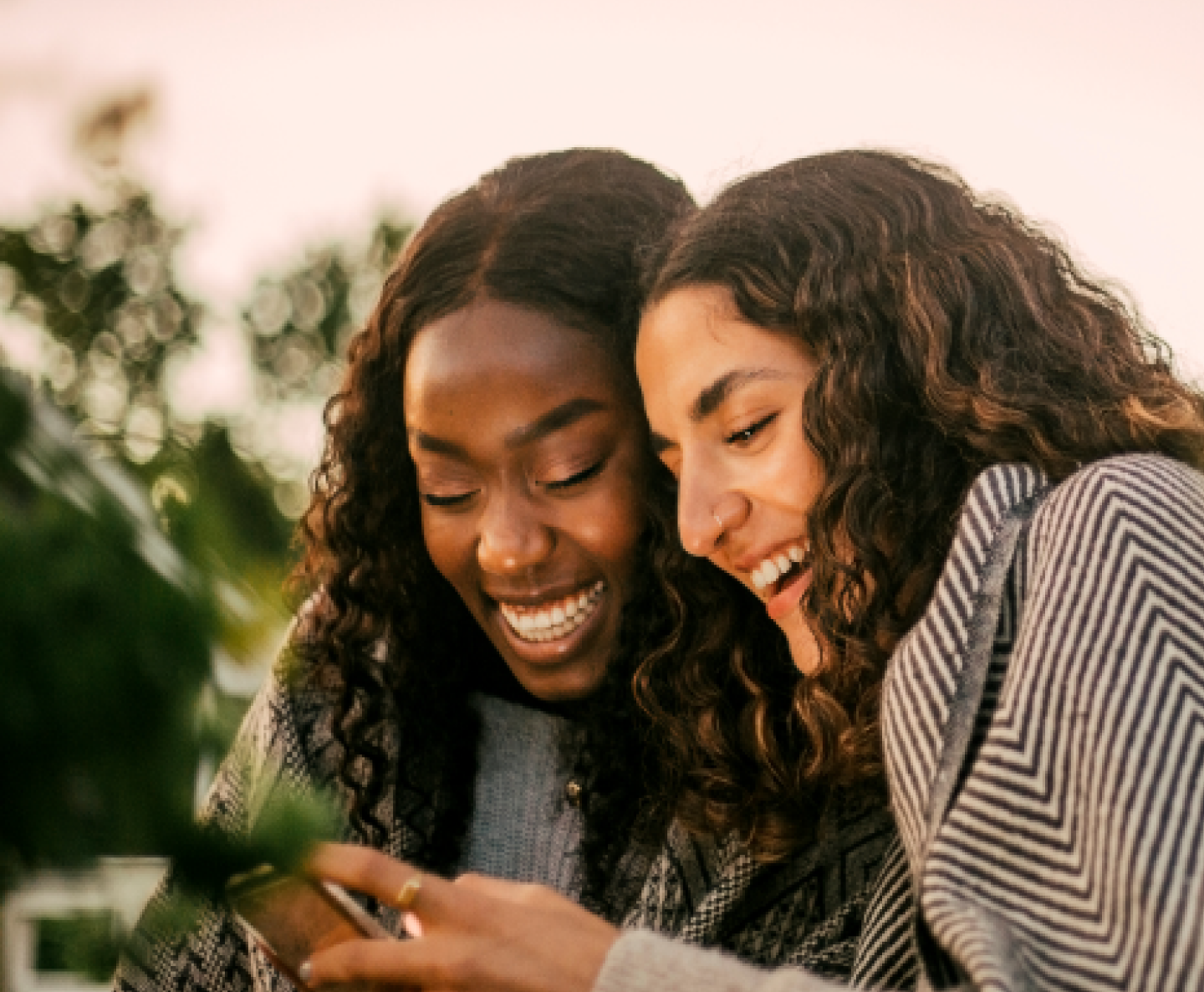 two friends with curly hair smiling looking at a mobile phone