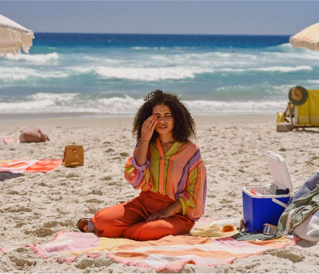 Woman sitting on the beach with her hand over her right eye in pain