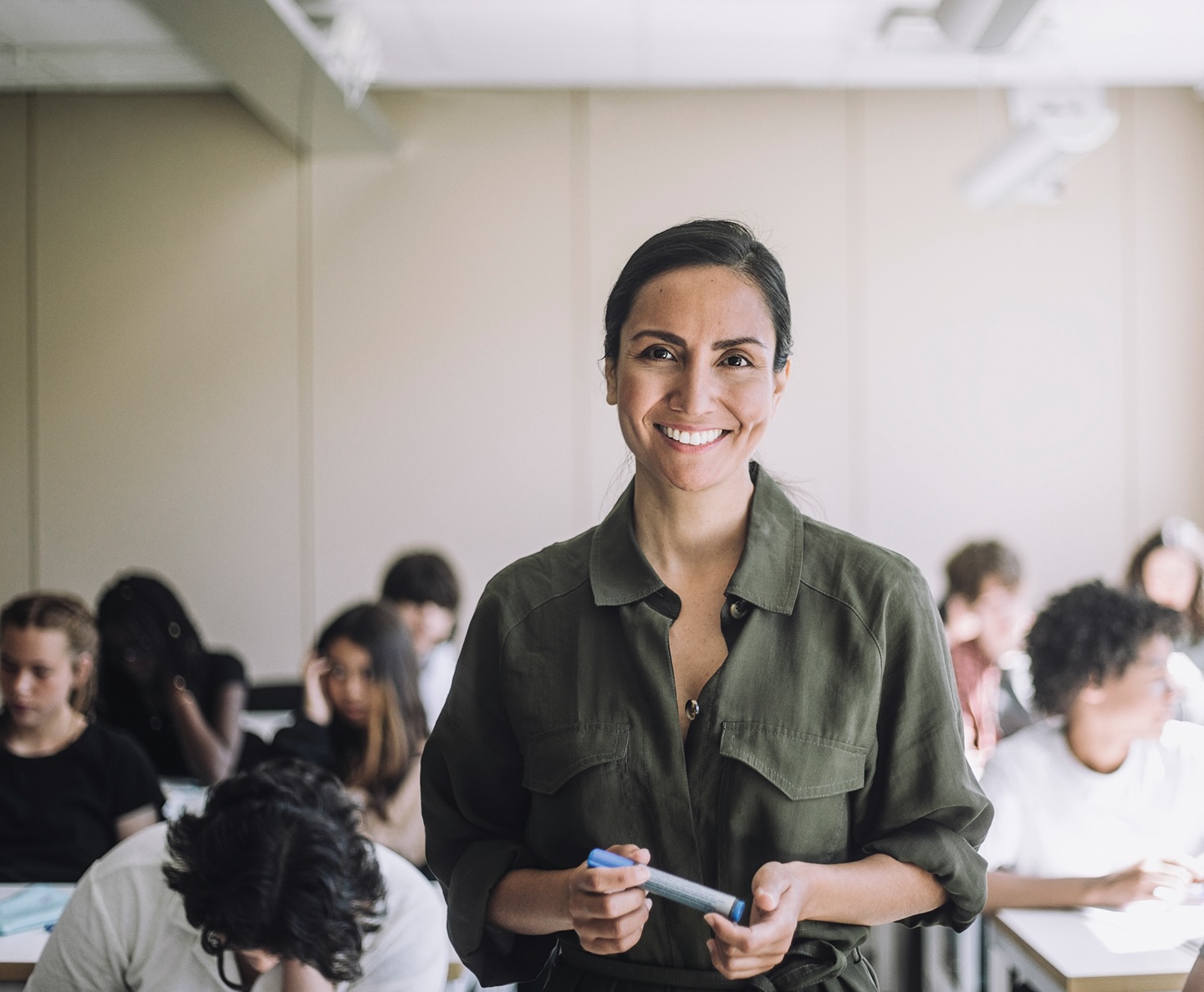 Smiling woman in a green shirt with a classroom in the background