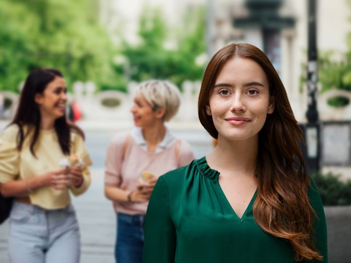 Smiling woman in a green blouse, with two women talking in the background