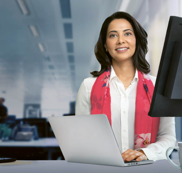 Mulher com camisa branca de botão e lenço vermelho sorrindo enquanto trabalha no laptop