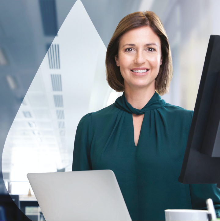 Frau in Business-Kleidung mit Laptop schaut lächelnd in die Kamera