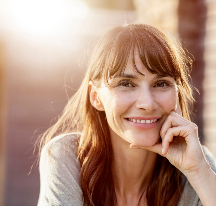 Γυναίκα με μακριά καστανά μαλλιά που χαμογελά κοιτάζοντας απευθείας στην κάμερα με χρυσό φως στο φόντο