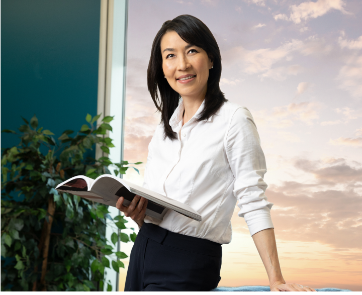 Woman with white button down shirt and black hair smiling while holding an open book