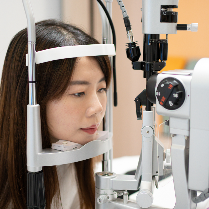 side perspective of patient taking an eye exam while resting her chin on a slit lamp device