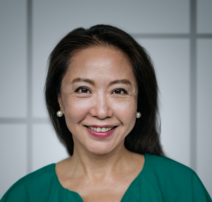 Woman smiling looking into camera wearing pearl earrings and green blouse