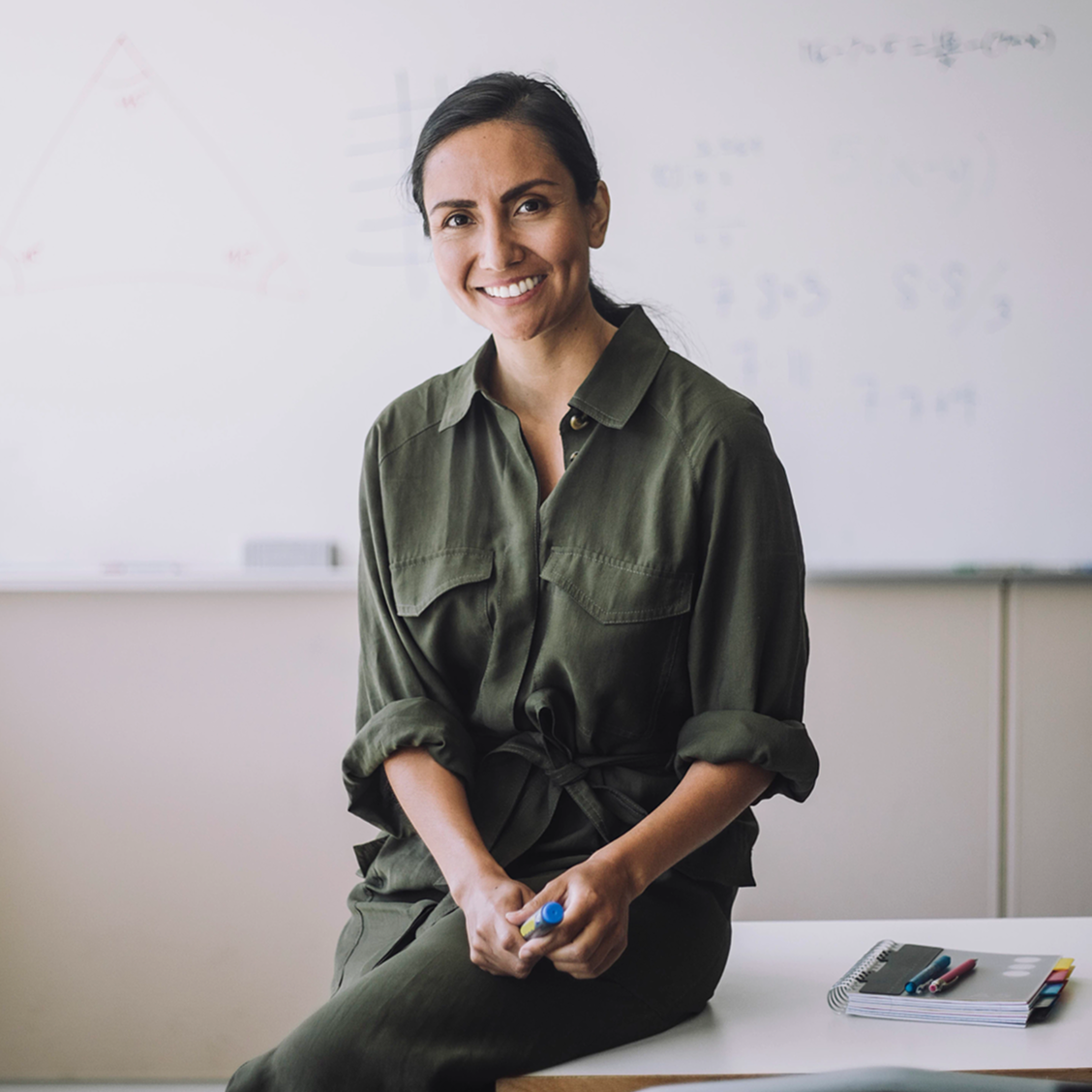 Smiling woman in a green shirt with a classroom in the background