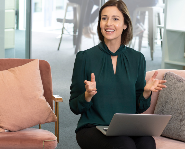 Kvinna med kort brunt hår och bärbar dator som pratar på ett kontor