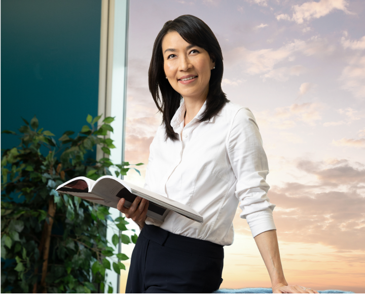Woman with white button down shirt and black hair smiling while looking at book