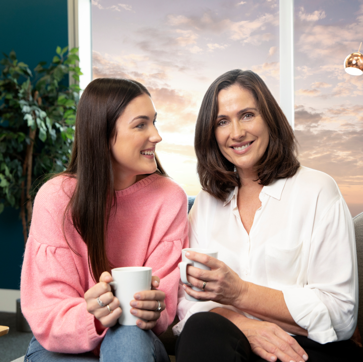 dve ženski sedita skupaj, se smejita in držita skodelici za kavo