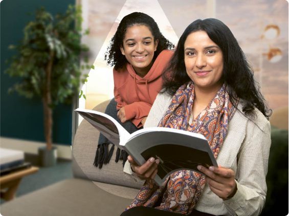 Lachende vrouw in wit hemd die een boek bekijkt met een jong meisje op achtergrond