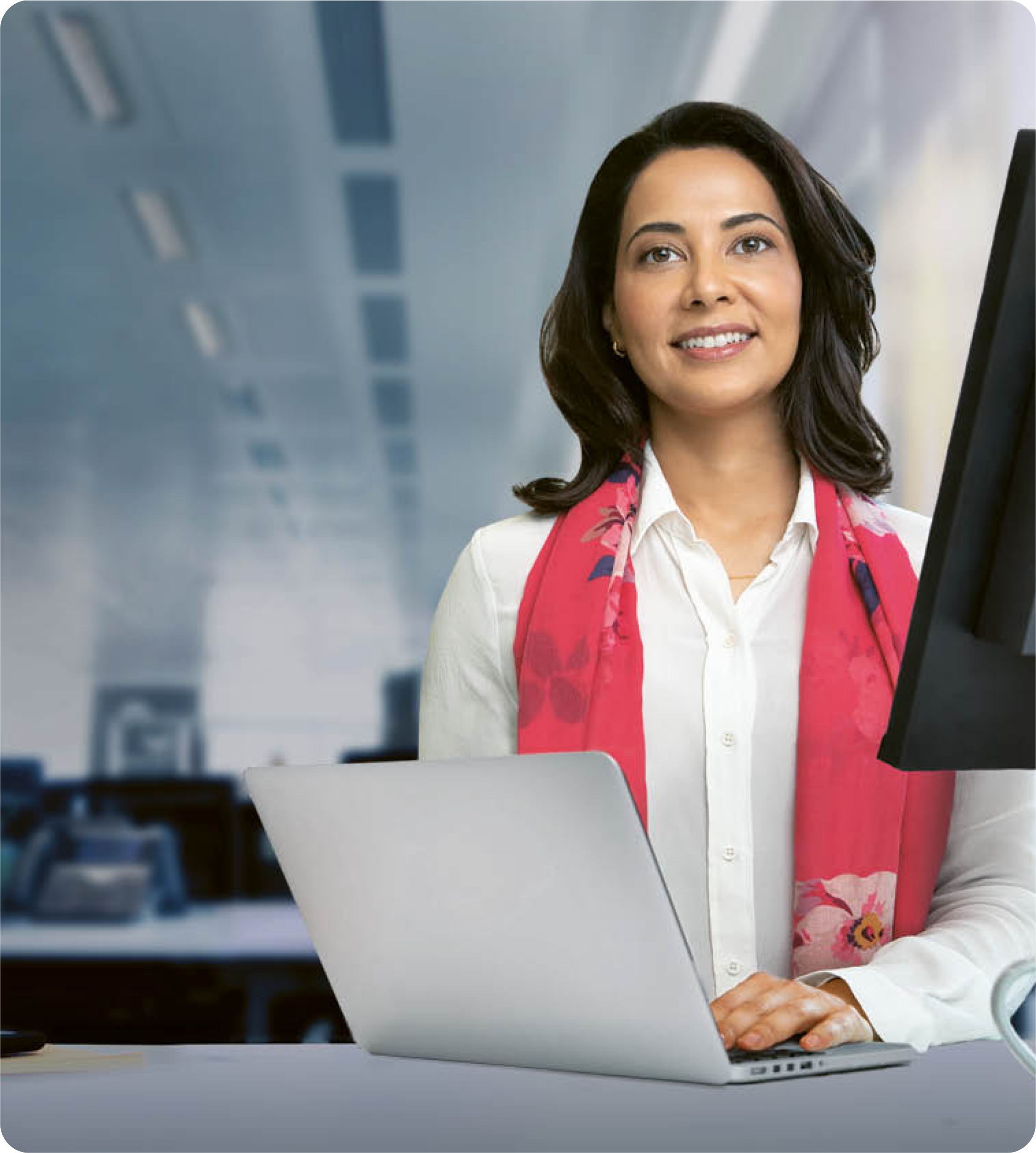 Mulher de camisa branca e lenço vermelho a sorrir enquanto trabalha ao computador