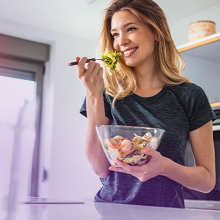 Woman smiling and eating a salad while holding a glass bowl