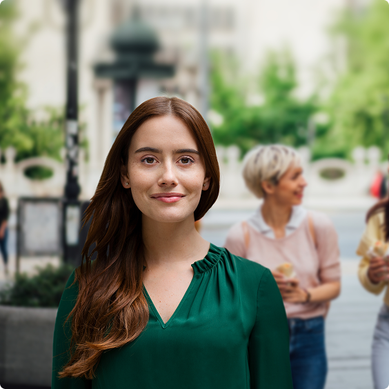 Smiling woman in a green blouse, with two women talking in the background